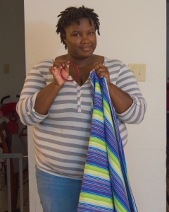 Brittany holding a red sling ring in her hand and a blue, green, white, and purple woven wrap in the other hand